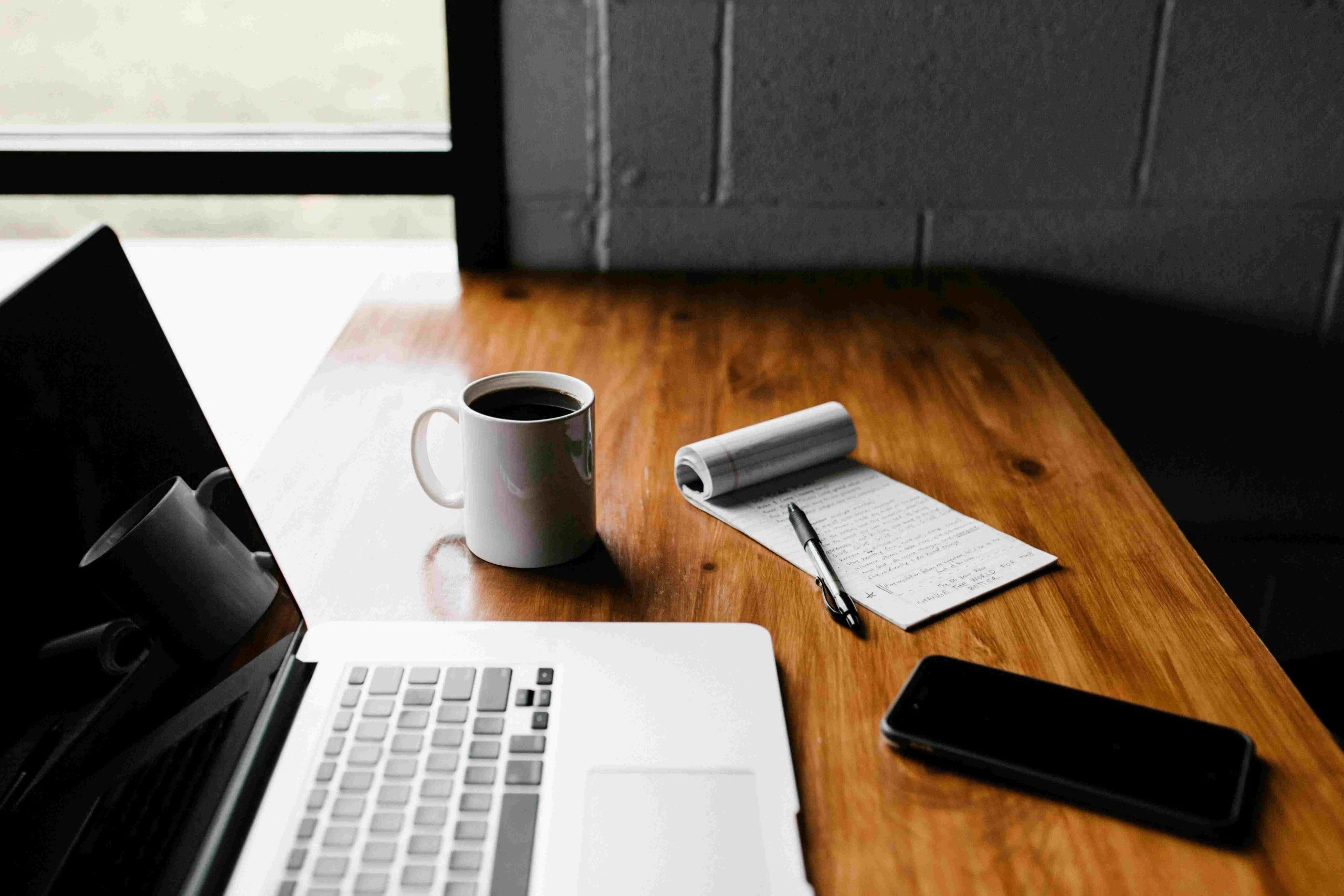 Laptop, mug, phone, notepad on table